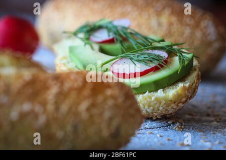 Primo piano di panino vegano a base di pane di mais con avocado, rafano e aneto su fondo nero cosparso di farina Foto Stock
