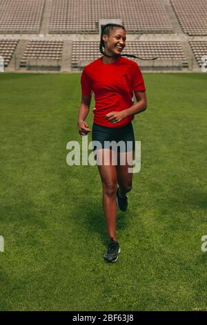 Sorridente femmina di calcio giocando a correre sul campo. Donna in uniforme allenamento sul campo di calcio. Foto Stock