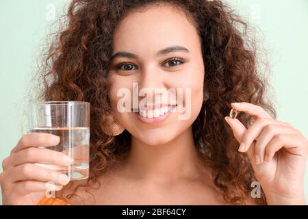 Giovane donna con olio di pesce e bicchiere d'acqua su sfondo colorato Foto Stock