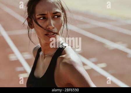 Primo piano di una donna sportiva dopo una corsa sulla pista dello stadio. Atleta femminile sicura in piedi sulla pista e guardando lontano. Foto Stock