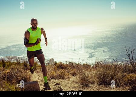 Tutta la lunghezza di uomo fitness che corre su sentiero roccioso in montagna. Montare il giovane uomo che corre su una collina. Foto Stock