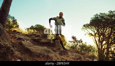 Uomo che corre sulle piste di montagna. fitness maschile che corre attraverso un sentiero roccioso di montagna. Foto Stock