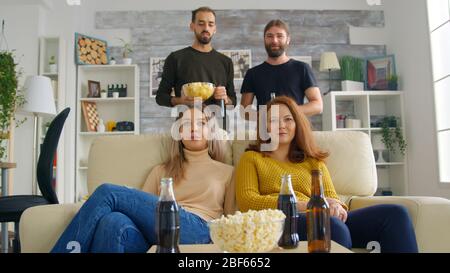 Giovane donna che arriva con la pizza per guardare una partita di calcio in tv con i suoi amici. Amici felici Foto Stock