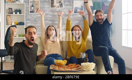 Gruppo di amici felici dopo la loro squadra di calcio preferita vince il campionato. Amici seduti sul divano mangiare pizza e patatine. Foto Stock