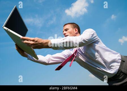 Uomo d'affari stressato che si sta avvicinando per prendere un computer portatile che cade dal cielo blu Foto Stock