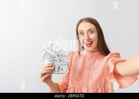 Giovane donna felice che prende selfie con i soldi su sfondo chiaro Foto Stock