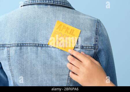 Donna che attacca la carta alla schiena del suo amico contro sfondo colore, closeup. Aprile Fool' Day prank Foto Stock