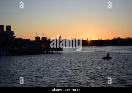 I pescatori solitari navigano nel mezzo di un fiume durante tramonto Foto Stock