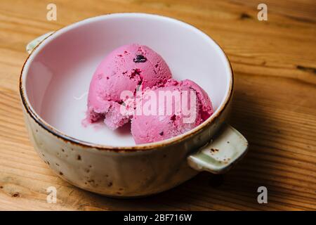 Due palline di gelato rosa in una ciotola su un tavolo di legno. Foto Stock