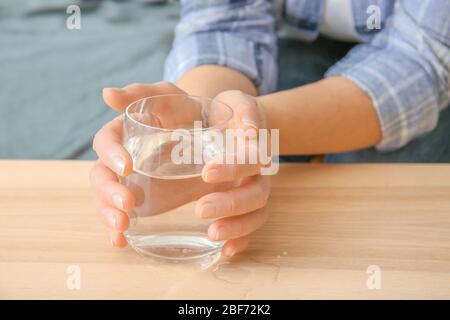 Donna anziana con sindrome di Parkinson bere acqua a casa, primo piano Foto Stock