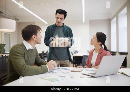 Gruppo di consulenti finanziari seduti al tavolo e ascoltati dal proprio manager durante una riunione in ufficio Foto Stock