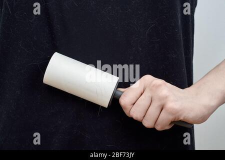 Una donna irriconoscibile pulisce una t-shirt nera con un rullo per abiti. Foto Stock