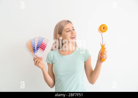 Giovane donna con campioni di colore e rullo di vernice su sfondo bianco Foto Stock