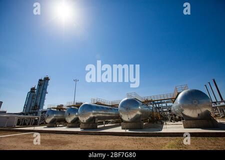 Raffineria di petrolio e impianto di lavorazione del gas nel deserto. Alcuni scambiatori di calore e torri di distillazione (colonne di raffineria) su cielo blu con sole. Foto Stock