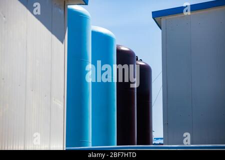 Primo piano delle attrezzature degli impianti petrolchimici. Impianto di raffineria di petrolio. Serbatoi blu e nero di metallo di deposito di acqua su sfondo blu cielo. Foto Stock