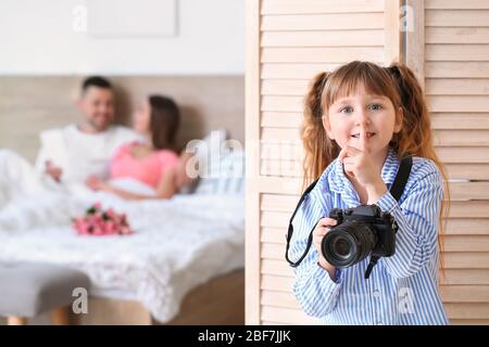 Bambina con fotocamera nascosta dietro schermo pieghevole in camera da letto dei genitori Foto Stock