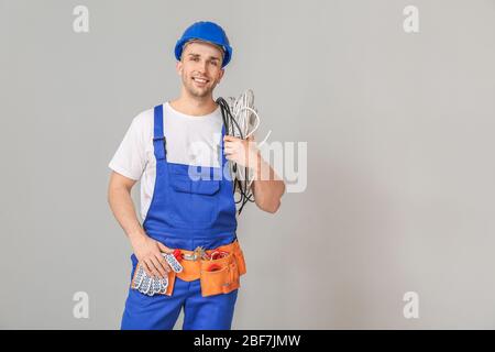 Bel lavoratore maschio con cavi su sfondo grigio Foto Stock