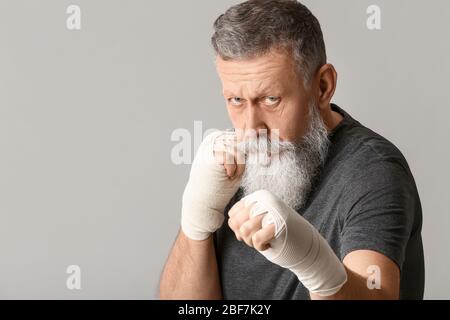 Uomo anziano sportivo con fasce da polso applicate su sfondo grigio Foto Stock