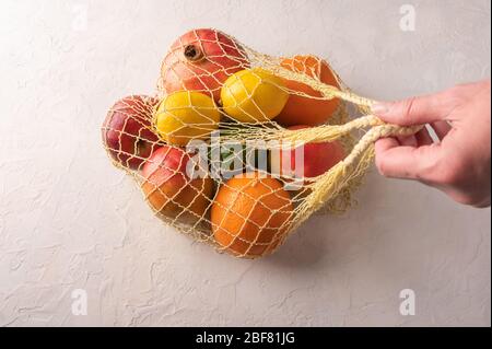 Donna mano tiene misto frutta organica, verdure e verdi in una borsa a stringa su sfondo chiaro. Concetto di ecologia aggiunta zero rifiuti Foto Stock