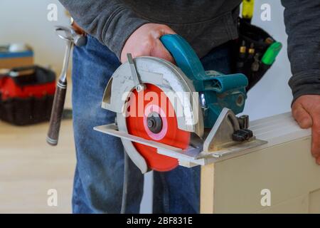 L'uomo mani tenendo la sega circolare e la preparazione di effettuare un taglio porta di legno per il processo di rimodellamento nuovo hous Foto Stock