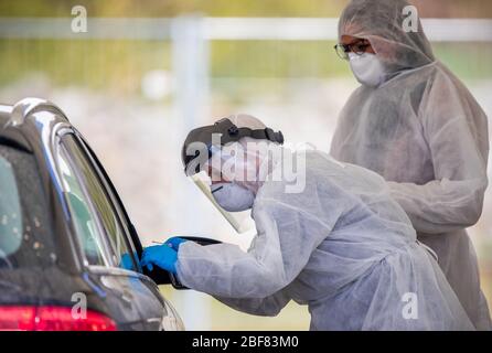 17 aprile 2020, Meclemburgo-Pomerania occidentale, Bützow: Utilizzando un tampone, Anja Hörichs, sostenuto da Stephanie Podojil (indietro), preleva un campione da un paziente in auto presso il centro di test per la sospetta corona. Il campione viene prelevato dalla gola del paziente. Fino a 50 campioni al giorno vengono prelevati presso il centro di test presso il reparto di manutenzione stradale. Foto: Jens Büttner/dpa-Zentralbild/dpa Foto Stock