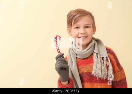 Carino ragazzo in abiti invernali e con canna da zucchero su sfondo colorato Foto Stock