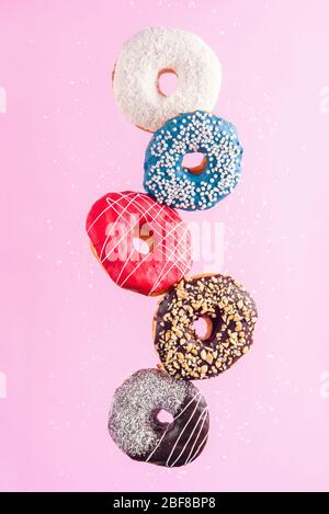 Ciambelle decorate multicolore in movimento cadendo su sfondo rosa. Ciambelle dolci che volano in movimento. Foto Stock
