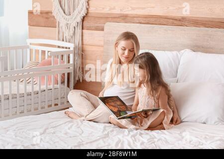 Bella donna incinta e la sua bambina lettura libro in camera da letto Foto Stock