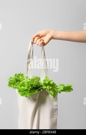 Mano femminile con lattuga fresca in borsa eco su sfondo colorato Foto Stock