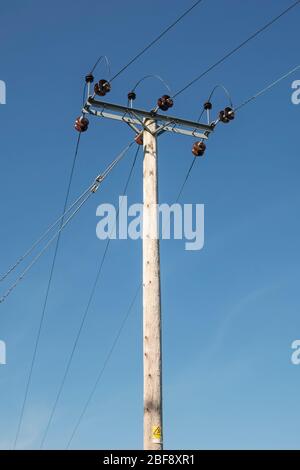 Un polo elettrico in legno ad alta tensione con isolatori in ceramica visti contro un cielo blu, nella campagna del Regno Unito Foto Stock