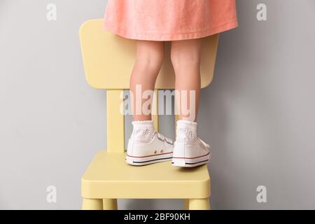 Piccola ragazza afro-americana in piedi sulla sedia vicino alla parete della luce. Bambini in pericolo Foto Stock