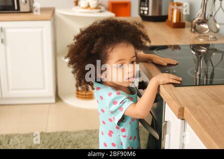 Piccola ragazza afro-americana che gioca con la stufa in cucina. Bambini in pericolo Foto Stock