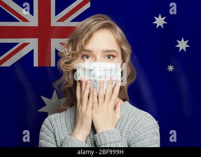 Donna scioccata in maschera medica sullo sfondo della bandiera australiana. Influenza epidemica e violenza domestica in Australia concetto Foto Stock