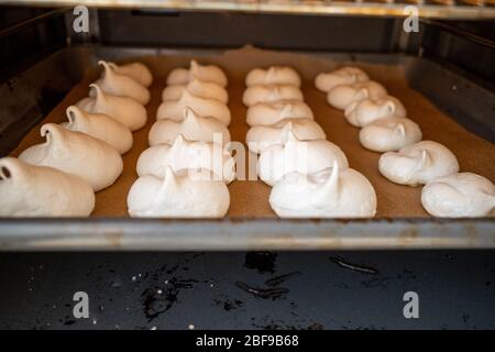 molte meringa appena sfornate si trovano su una teglia nel forno Foto Stock
