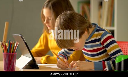 Apprendimento a distanza dei bambini a casa durante il periodo di quarantena del coronavirus Covid 19. Sorella e fratello fanno i compiti su un notebook. In primo piano c'è un ragazzo con una matita in mano. Foto Stock