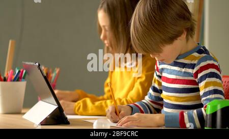 Apprendimento a distanza per gli scolari durante il periodo di quarantena del coronavirus. I bambini sono seduti al tavolo. Una ragazza e un ragazzo fanno i loro compiti in modo indipendente su un notebook. Foto Stock