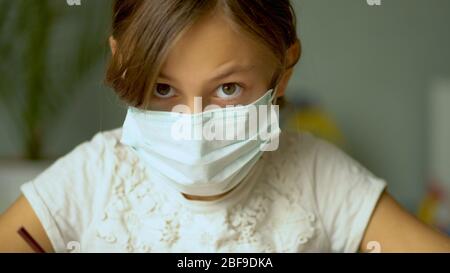 Formazione a domicilio durante il periodo di quarantena del Coronavirus Covid19. Una ragazza in una maschera medica protettiva fare i compiti. Vista ravvicinata. Foto Stock