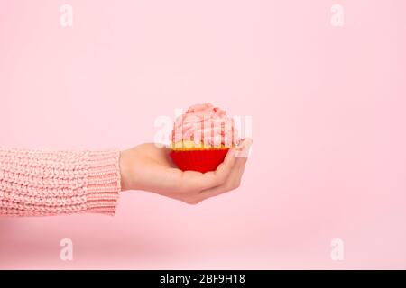 Gustoso cupcake su mano femminile su sfondo rosa chiaro. Concept festivo monocromatico con cupcake e glassa rosa. Spazio di copia. Foto Stock