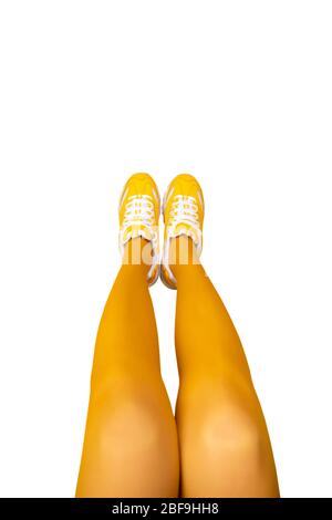 Nuove sneaker gialle femminili su lunghe gambe donna in collant gialli isolati su sfondo bianco. Concetto di pop art monocromatico. Banner verticale con copia spa Foto Stock