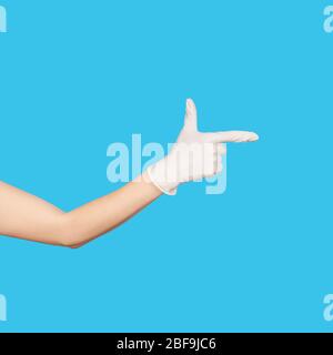 Cartello con la mano con la pistola. Mano in un guanto in lattice monouso bianco isolato su blu. Gesto della mano della donna o segno isolato su bianco. Foto Stock