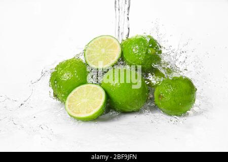 Acqua che si versa su lime fresche su sfondo bianco Foto Stock