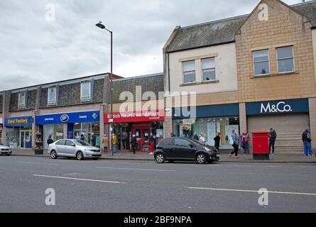 Musselburgh, High Street, East Lothian, Scozia, Regno Unito. Pavimenti molto silenziosi a causa del Coronavirus Lockdown, ma diverse auto di passaggio. La zona più trafficato per i pedoni era fuori Boots Pharmacy, (il chimico), nella foto, dove la gente era divulgente sociale in coda. Foto Stock