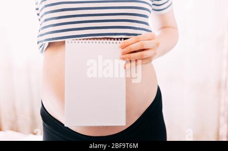 Allegra donna incinta che fa note in jotter, focuse sulla carta, pancia è non messa a fuoco Foto Stock
