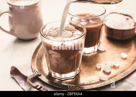 Versare il latte in un bicchiere di gustoso caffè ghiacciato sul tavolo Foto Stock