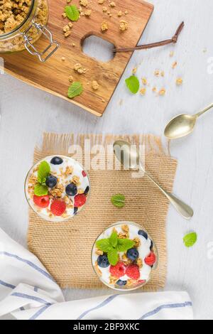 Mirtilli e lamponi di granola yogurt fatto in casa in vetro su sfondo di legno bianco chiaro. Concetto di cibo sano. Foto Stock