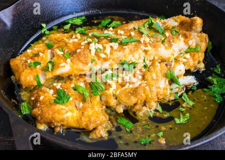 Merluzzo al forno con limone e aglio: Filetto di pesce bianco impanato con aglio tritato e prezzemolo in una padella di ghisa Foto Stock