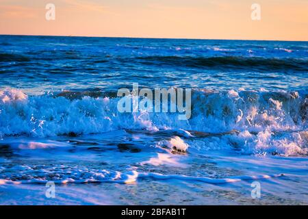 Incredibile tramonto sulla spiaggia con incredibili onde scintillanti. Tramonto e onde di mare sulla spiaggia spettacolare. Blu e giallo infinito Foto Stock