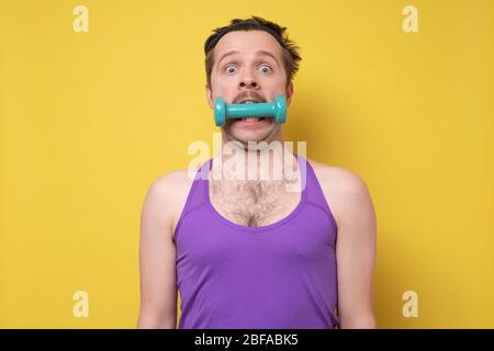 Giovane uomo sportivo che tiene un manubro in bocca. Esercizio divertente o concetto di denti sani. Foto Stock