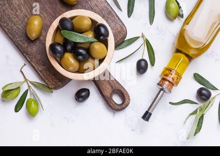 Olive nere e verdi in ciotola di legno e bottiglia di olio su tavola di marmo bianco, Foto Stock