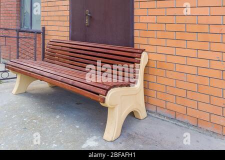 Una panca di legno seduta di fronte alla porta su un edificio in mattoni con una finestra rotta. Foto Stock